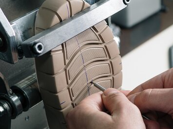 Zwei Hände prüfen die Sohle eines Schuhs in einer Maschine. | © Gabor Shoes GmbH, Rosenheim