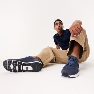 Ein Mann sitzt entspannt auf dem Boden, trägt beigefarbene Hose, blaues Oberteil und dunkelblaue Sneaker. Die Schuhe sind prominent im Vordergrund des Bildes zu sehen. | © Gabor Shoes GmbH, Rosenheim