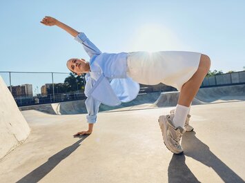 Una donna con abbigliamento chiaro e sneakers sportive compie un movimento dinamico in uno skatepark sotto il sole. | © Gabor Shoes GmbH, Germania