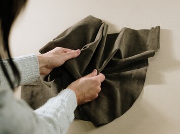 Zwei Hände halten und fühlen an einem Stück braunem Lederstoff. | © Gabor Shoes GmbH, Rosenheim