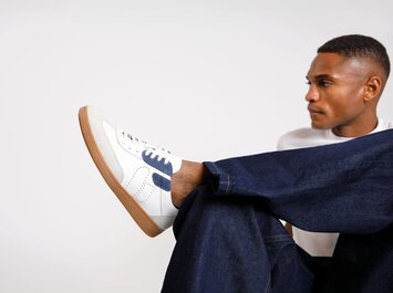 Un uomo indossa sneaker bianche con dettagli blu e suola marrone, abbinati a dei jeans blu scuro. La scarpa è ben visibile in primo piano. | © Gabor Shoes GmbH, Germania
