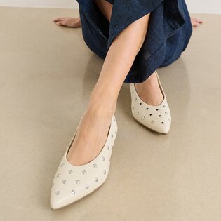 Eine Frau sitzt auf dem Boden und trägt eine dunkelblaue Hose sowie beigefarbene, spitze Pumps mit silbernen Nieten. | © Gabor Shoes GmbH, Rosenheim