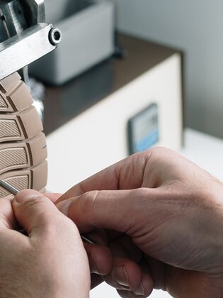 Primo piano di mani che lavorano una suola chiara di una scarpa su un dispositivo metallico. | © Gabor Shoes GmbH, Germania