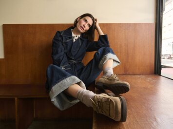 Eine Frau  liegt auf dem Boden und trägt eine dunkelbraune, geflochtene Ballerina aus Leder, kombiniert mit einer dunklen Jeans. Der Fokus liegt auf dem Schuh. | © Gabor Shoes GmbH, Rosenheim