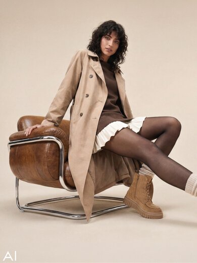 Ein mit KI generiertes Bild, dass eine Frau zeigt, die auf einem Ledersessel vor beigefarbenem Hintergrund sitzt. Sie trägt einen hellbraunen Trenchcoat über einem dunkelbraunen Oberteil und weißem Faltenrock und hat beige Gabor-Schnürboots an. | © Gabor Shoes GmbH, Rosenheim