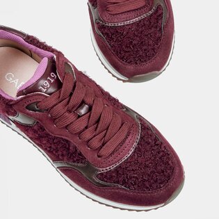 Eine Frau mit beigefarbener Hose trägt bordeauxrote Sneaker und steht vor zwei Spiegeln, sodass die Schuhe mehrfach reflektiert werden. | © Gabor Shoes GmbH, Rosenheim