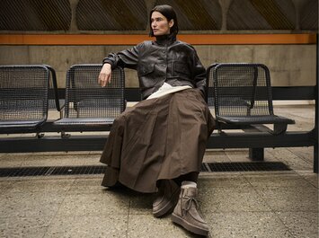 Eine Frau sitzt auf einer Bank in einer U-Bahn-Station, trägt eine braune Lederjacke, langen braunen Rock und beigefarbene Gabor-Schnürboots. | © Gabor Shoes GmbH, Rosenheim