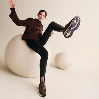 Eine Frau macht eine dynamische Pose auf einem Skatepark, trägt ein hellblaues Hemd, einen weißen Rock und beige Turnschuhe. | © Gabor Shoes GmbH, Rosenheim