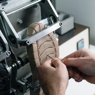 Zwei Hände prüfen die Sohle eines Schuhs in einer Maschine. | © Gabor Shoes GmbH, Rosenheim