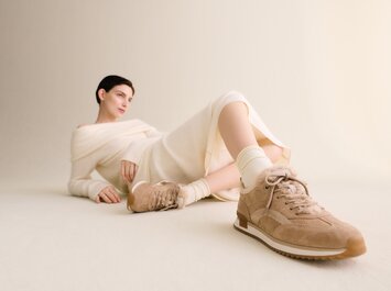 Eine Frau liegt entspannt auf dem Boden vor hellem Hintergrund, trägt ein cremefarbenes Strickkleid und beigefarbene Gabor-Sneaker mit heller Sohle. | © Gabor Shoes GmbH, Rosenheim