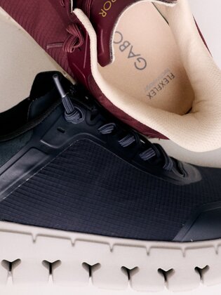 Eine Frau sitzt auf dem Boden und trägt rosa Sneakers mit weißen und rosafarbenen Socken. Die Hand berührt die Schuhsohle, der Hintergrund ist weiß und schlicht. | © Gabor Shoes GmbH, Rosenheim