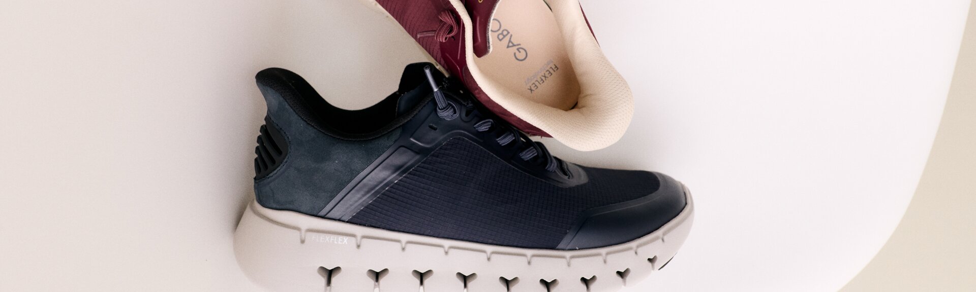 Eine Frau sitzt auf dem Boden und trägt rosa Sneakers mit weißen und rosafarbenen Socken. Die Hand berührt die Schuhsohle, der Hintergrund ist weiß und schlicht. | © Gabor Shoes GmbH, Rosenheim