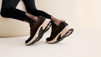 Eine Frau sitzt vor einem weißen Hintergrund, hält das Bein ausgestreckt und trägt weiße Sneaker mit gelben Details. | © Gabor Shoes GmbH, Rosenheim