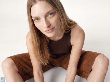 Ein mit KI generiertes Bild, das eine junge Frau zeigt, die lässig am Boden sitzt und ein dunkelbraunes Top mit brauner kurzer Hose trägt. | © Gabor Shoes GmbH, Rosenheim