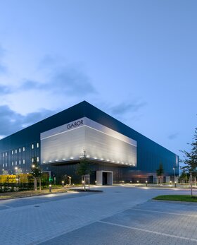 Modernes Firmengebäude von Gabor bei Dämmerung mit beleuchtetem Vorplatz und Gabor-Schriftzug. | © Gabor Shoes GmbH, Rosenheim
