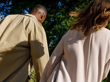Two people in light coats walking outdoors in greenery. | © Gabor Shoes GmbH, Germany